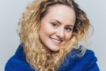 Wall Mural - Close up shot of attractive young woman with light crisp hair, blue eyes and shining smile, looks positively at camera, being in good mood after walk outdoor, isolated over light blue background