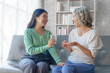 © NanSan - 60s asian mother elderly sitting on sofa with young asia female daughter together in living room. give medicine and water