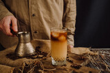 Fototapeta Na sufit -  a glass of refreshing cold coffee with ice and milk is standing on a wooden table near a male barista 2