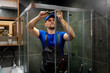 Young man in uniform repairs the shower door in the bathroom. A male repairman repairs the shower cabin. 