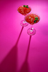 Two glasses with an alcoholic cocktail on a pink background