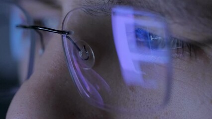 Female eyes in eyeglasses late at night scrolling in front of laptop. Coder, programmer or developer using laptop in dark. Close up of glasses with reflection of computer screen. 4K resolution