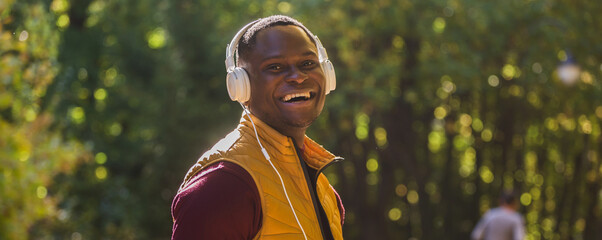 Banner portrait African american man listens music in summer park background copy space. Gadget, app and streaming service concept