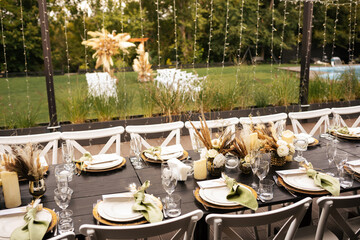 Wedding decorations. Served wedding table with golden plates, green napkins, decorative fresh and dried flowers, candles and and light bulbs. Celebration details, wedding outdoor