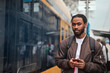 © olly - young man at the tram station with a phone in hand