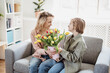 © candy1812 - Mother and daughter sitting on the sofa with tulips in their hands indoor.