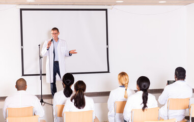 Wall Mural - Confident male speaker in white coat giving presentation from stage at medical conference