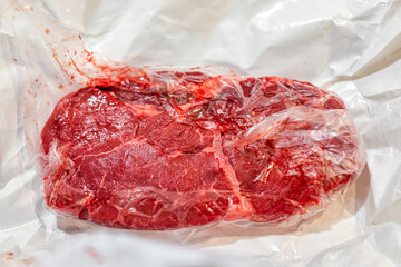 Uncooked raw red sirloin or ribeye steak cut macro closeup of texture wrapped in paper plastic wrap packaging from butcher