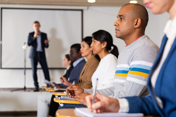 Wall Mural - Concentrated Hispanic man sitting in conference room listening to lecturer and making notes during business training