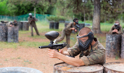 Wall Mural - Paintball player in camouflage and mask aiming with gun in shootout outdoors