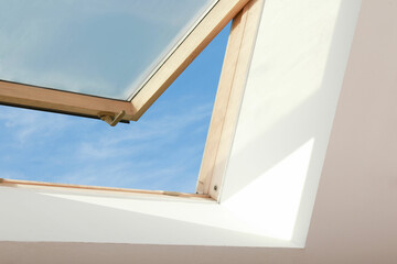 Open skylight roof window on slanted ceiling in attic room