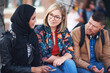 © moose/peopleimages.com - Friends, diversity and happy people with communication and connection outdoor on stairs. Hijab, muslim and talking women and adult learning and international student community on college steps
