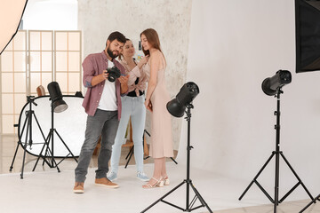 Poster - Male photographer and his assistant working with beautiful model in studio