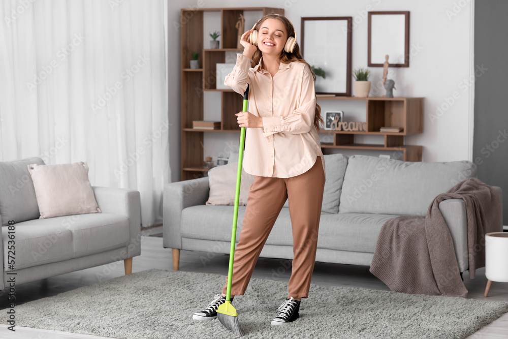 Young woman in headphones sweeping at home