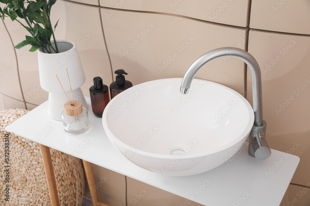 Ceramic sink, reed diffuser and liquid soap on table near tile wall