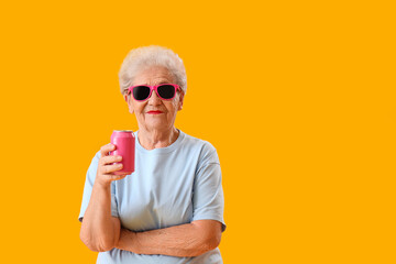 Canvas Print - Senior woman in sunglasses with can of soda on yellow background