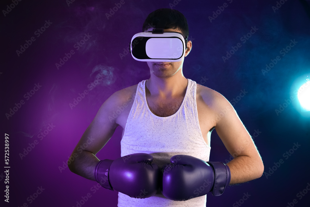 Young man with VR glasses and boxing gloves on color background