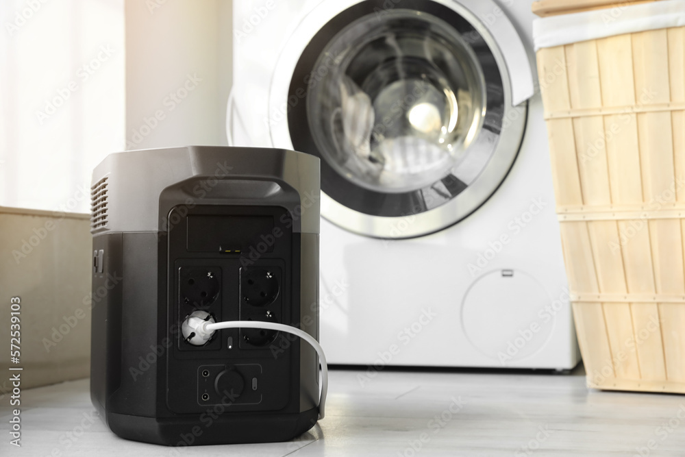Washing machine plugged in portable power station in laundry room, closeup