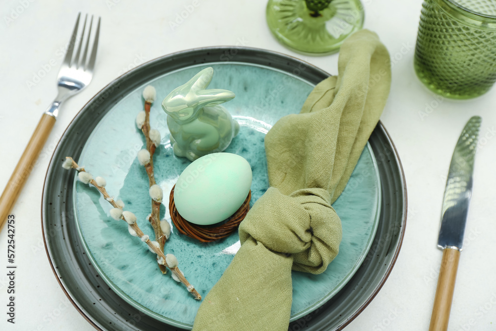 Stylish table setting with Easter egg, willow branches and ceramic bunny on light background, closeup