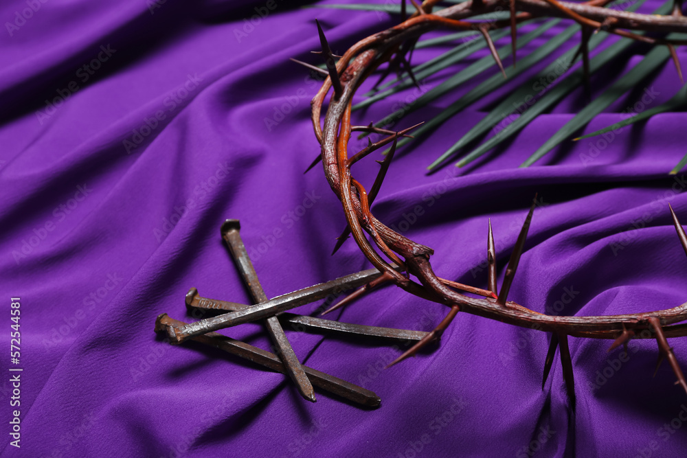 Crown of thorns with nails and palm leaf on purple fabric background. Good Friday concept