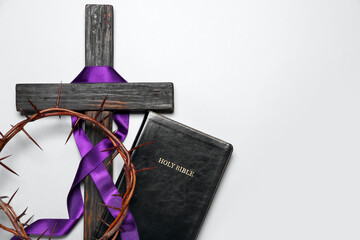 Wooden cross with purple ribbon, crown of thorns and Holy Bible on light background. Good Friday concept