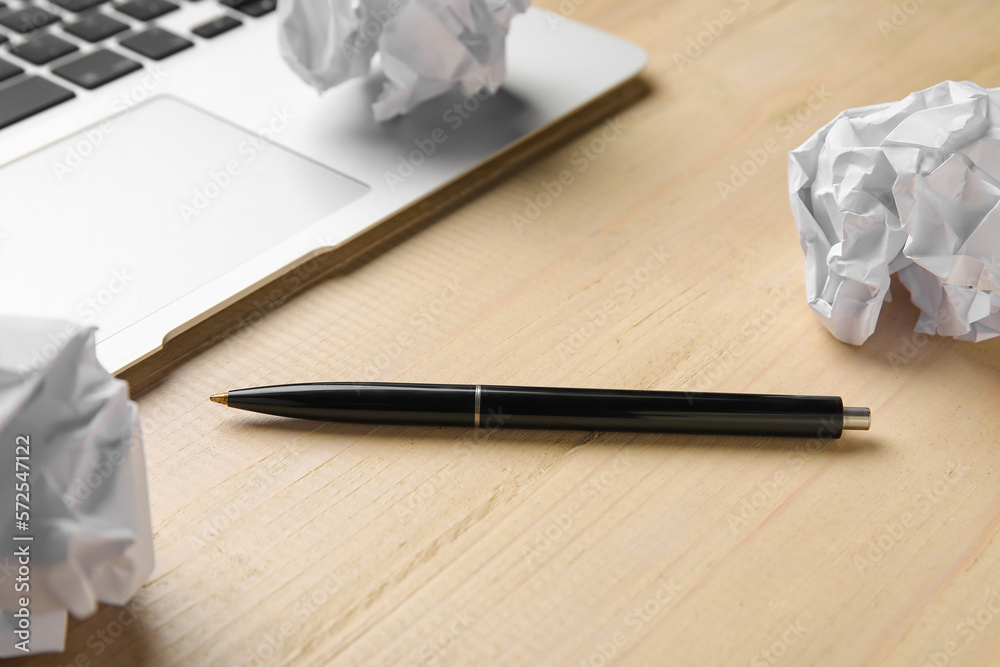 Pen, crumpled paper balls and laptop on wooden table, closeup. World Poetry Day celebration
