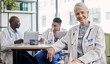 © Jordan C/peopleimages.com - Senior woman, doctor and portrait at hospital desk with smile for healthcare, planning surgery and teamwork. Leader, doctors and experience in health, wellness and happy in clinic with group at table