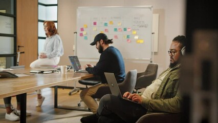 Wall Mural - Male software developer sitting in a boardroom and working on a code. Creative business man working on a laptop in an office. Man working in a tech company with his colleagues.