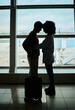 © Nina Lawrenson/peopleimages.com - Silhouette, travel and love with couple in airport and hug for departure, flight and say goodbye. Shadow, holiday and sad man and woman leave in embrace by window for journey, international