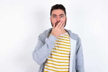 Wall Mural - Emotional caucasian man wearing casual sportswear over white wall gasps from astonishment, covers opened mouth with palm, looks shocked at camera.