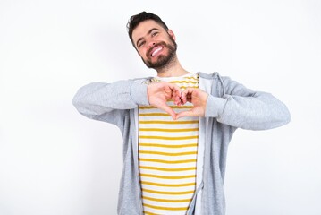 caucasian man wearing casual sportswear over white wall smiling in love doing heart symbol shape with hands. Romantic concept.