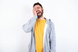 © Jihan - caucasian man wearing casual sportswear over white wall makes face palm and smiles broadly, giggles positively hears funny joke poses