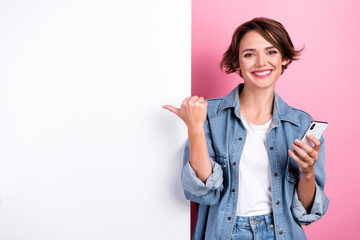 Portrait of charming positive person hold telephone indicate finger empty space banner isolated on pink color background