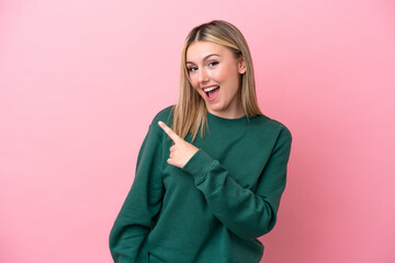 Young caucasian woman isolated on pink background surprised and pointing side