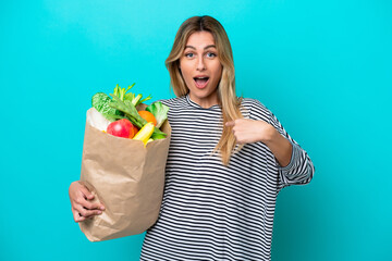 Wall Mural - Young Uruguayan woman holding a grocery shopping bag isolated on blue background with surprise facial expression