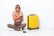 © luismolinero - Uruguayan traveler woman sitting on the floor isolated on white background pointing to the laterals having doubts