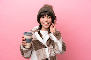 Sticker - Little caucasian girl with winter jacket isolated on pink background holding coffee to take away and a mobile