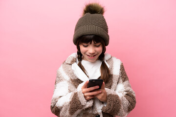 Sticker - Little caucasian girl with winter jacket isolated on pink background sending a message with the mobile