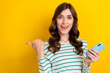 Sticker - Photo portrait of lovely young lady hold gadget excited point empty space wear trendy striped outfit isolated on yellow color background