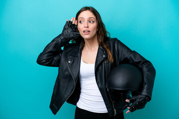 Wall Mural - Young caucasian woman with a motorcycle helmet isolated on blue background listening to something by putting hand on the ear