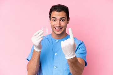 Wall Mural - Dentist caucasian man holding invisible braces isolated on pink background doing coming gesture