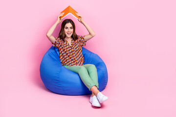 Sticker - Full length photo of young childish playful girl student sitting bean bag make book house protection carefree isolated on pink color background