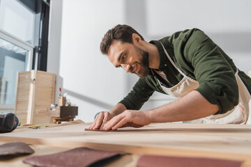 Wall Mural - Smiling bearded workman sanding wooden board in workshop.