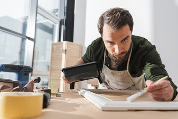 Wall Mural - Bearded repairman painting on wooden picture frame in workshop.