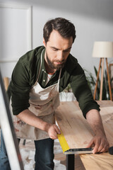 Wall Mural - Bearded carpenter using square tool on wooden board in workshop.