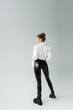 back view of sexy woman in black latex pants and rough boots standing on grey background.