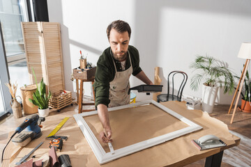 Wall Mural - Bearded restorer painting on wooden picture frame near tools in workshop.