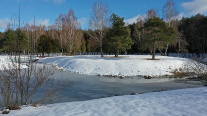 An island with large trees in the middle of a frozen river like in a fairy tale in winter under a layer of snow. Mountain lake covered with blue ice. Ecotrail. Hydropark under the ice.