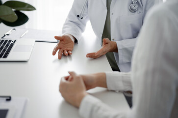 Doctor and patient discussing current health examination while sitting at the desk in clinic office, closeup. Perfect medical service and medicine concept