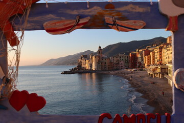 Wall Mural - Camogli, Italy - January 27, 2023: Beautiful old mediterranean town at the sunrise time with illumination during winter days. People enjoying the evening at the beach with beautiful sunset background